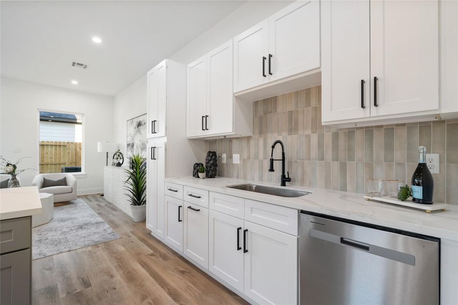 The undermount farmhouse-style sink is tucked to the side, surrounded by ample soft-close cabinetry for generous storage. A striking backsplash in a mix of light green and earthy brown tones adds warmth and character to the space. This thoughtful design perfectly balances functionality with modern farmhouse charm