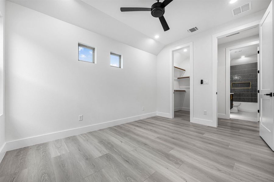 Unfurnished bedroom with vaulted ceiling, light wood-style flooring, baseboards, and a walk-in closet. Unfurnished bedroom with vaulted ceiling, light wood-style flooring, baseboards, and a walk-in closet.