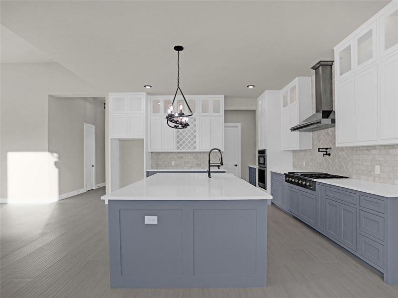 Kitchen with wall chimney range hood, white cabinetry, black gas cooktop, an island with sink, and decorative light fixtures