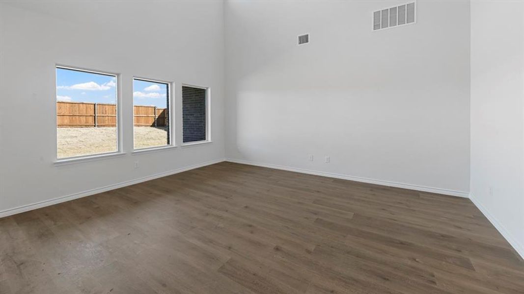 Spacious room featuring vaulted ceilings, light wood-finish flooring, white baseboards, and three rectangular windows Spacious room featuring vaulted ceilings, light wood-finish flooring, white baseboards, and three rectangular windows