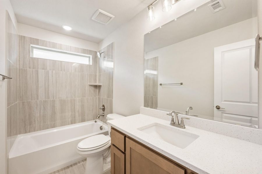 Bathroom with tiled tub-shower combo, white quartz vanity, and large mirror above single sink Bathroom with tiled tub-shower combo, white quartz vanity, and large mirror above single sink