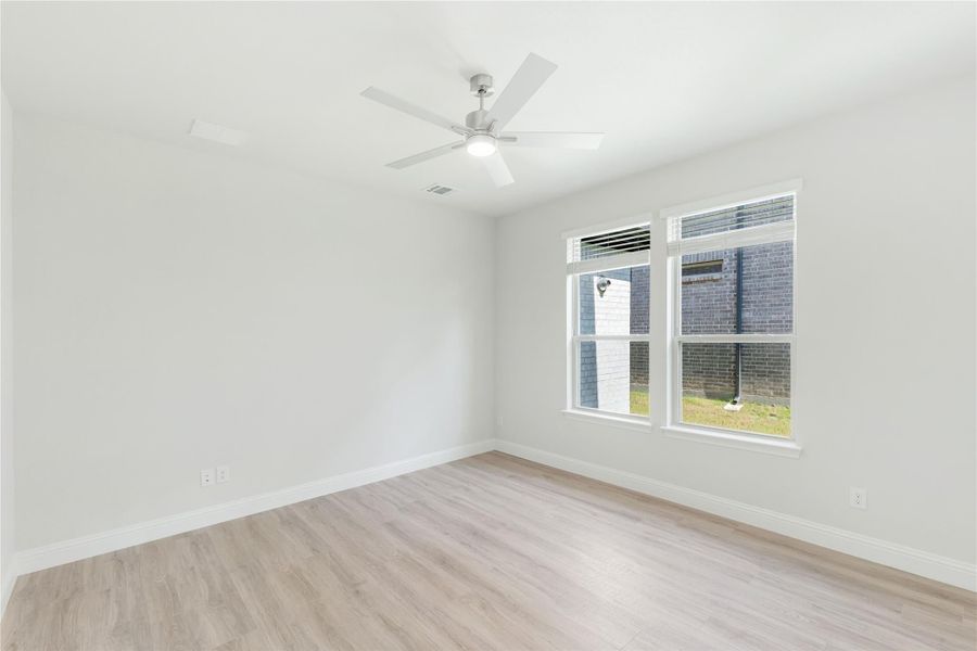 Empty bedroom with light wood floors, ceiling fan, and double windows with natural light
