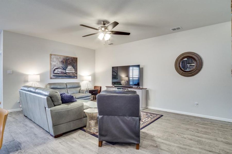 Living room featuring light wood finished floors, visible vents, baseboards, and a ceiling fan