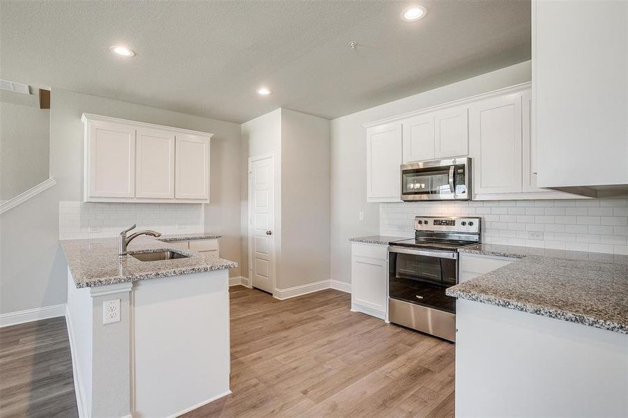 Kitchen featuring stainless steel appliances, a peninsula, light stone counters, backsplash, and white cabinets