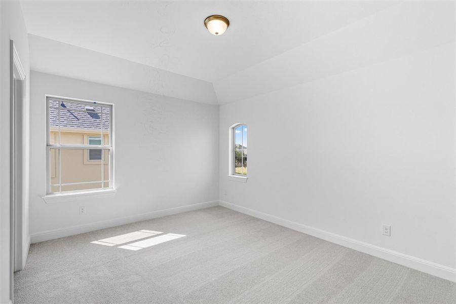 Empty room with light colored carpet, plenty of natural light, and vaulted ceiling