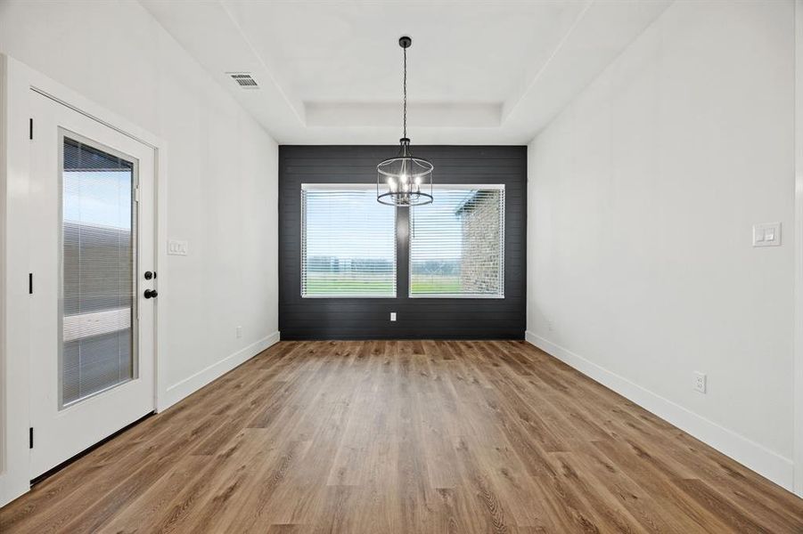 Unfurnished dining area with baseboards, visible vents, a raised ceiling, wood finished floors, and an inviting chandelier