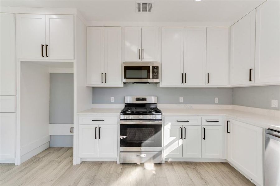 Kitchen with light hardwood / wood-style floors, white cabinets, and appliances with stainless steel finishes