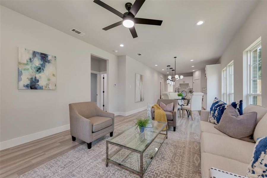 Living room with ceiling fan with notable chandelier and light hardwood / wood-style flooring