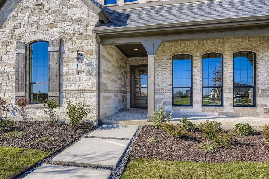 Doorway to property with a porch, a shingled roof, and stone siding