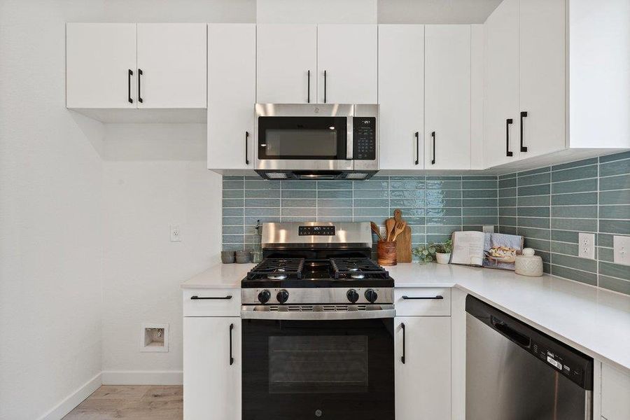 Modern kitchen featuring white cabinetry, stainless steel appliances, a white countertop, and a blue subway tile backsplash