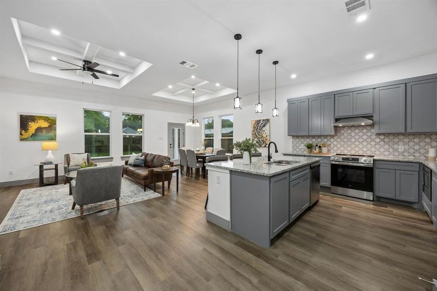 Open-concept living space featuring a kitchen island with granite countertops, gray cabinetry and stainless steel appliances