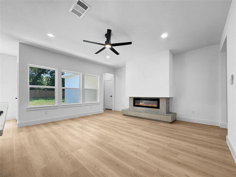 Unfurnished living room with a tile fireplace, a ceiling fan, light wood-style floors, recessed lighting, and a textured ceiling