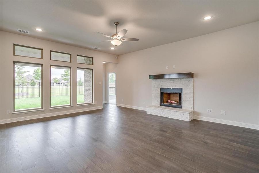 Unfurnished living room featuring ceiling fan, a brick fireplace, and dark hardwood / wood-style flooring