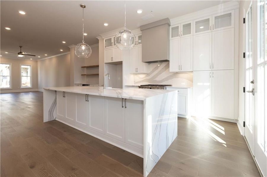 Kitchen featuring white cabinetry, light stone counters, ceiling fan, a spacious island, and custom range hood