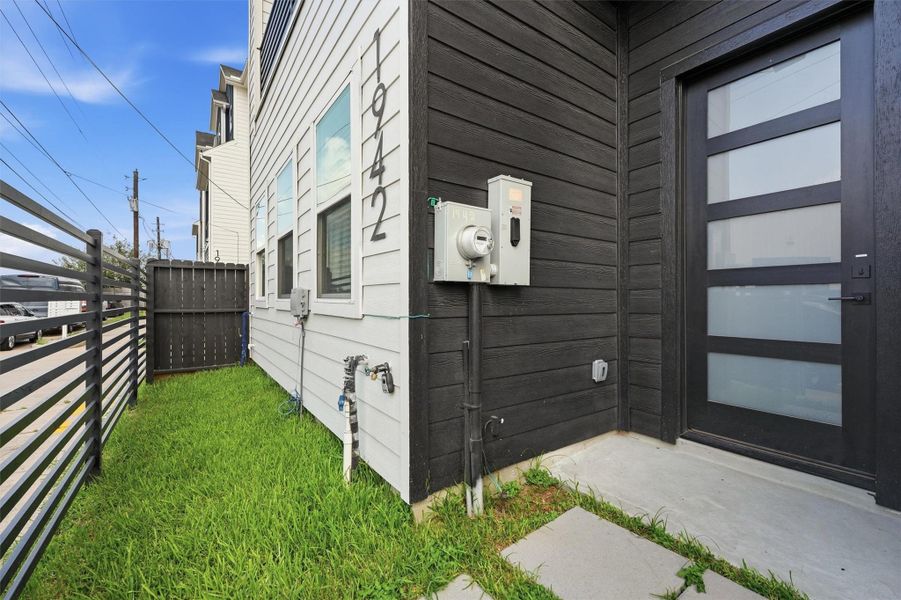 Side yard entry highlights a private fenced green space, contemporary exterior finishes, and a sleek modern front door for added curb appeal.