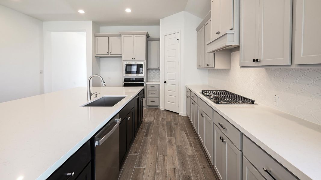Kitchen with backsplash, wood finish floors, recessed lighting, gray cabinets, and appliances with stainless steel finishes Kitchen with backsplash, wood finish floors, recessed lighting, gray cabinets, and appliances with stainless steel finishes