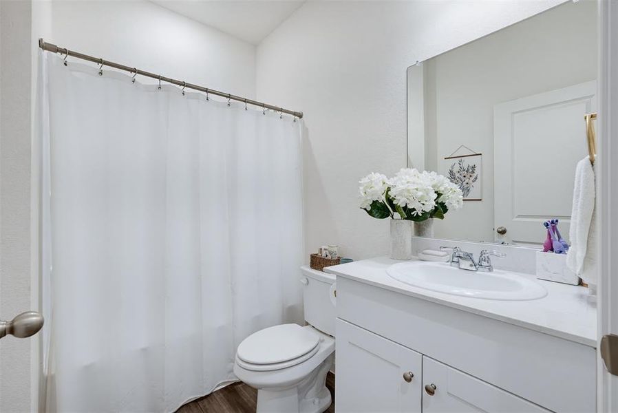 Bathroom featuring a single vanity with a white countertop and integrated sink, chrome faucet, white cabinetry with brushed nickel hardware, and wood-finish flooring