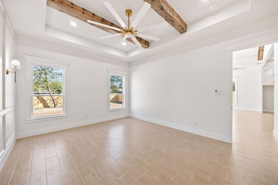 Spare room featuring beam ceiling, a tray ceiling, recessed lighting, wood tiled floors, and healthy amount of natural light