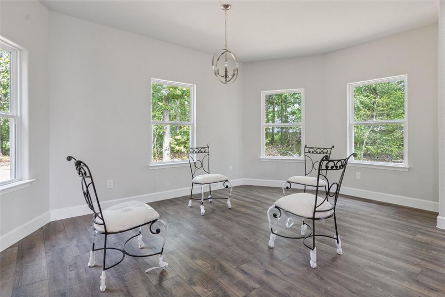 Bright, airy room with large windows offering scenic views of greenery. Features elegant flooring and a modern light fixture, perfect for a cozy sitting area or dining space.