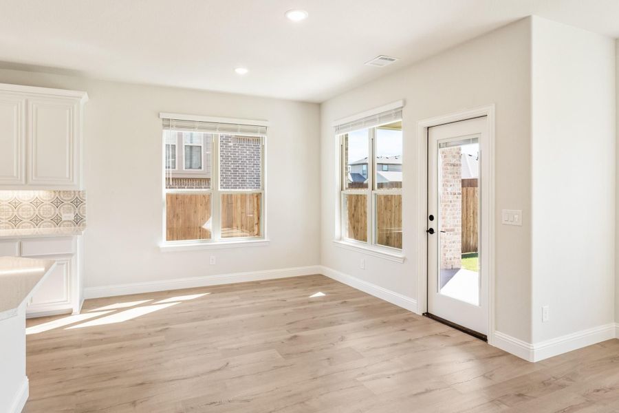Bright dining area with light wood floors, two windows, and a glass back door leading outside