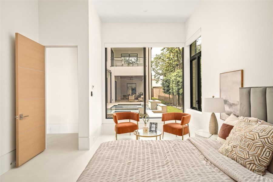 Light-filled bedroom with a seating area and large windows overlooking the pool and outdoor spaces.