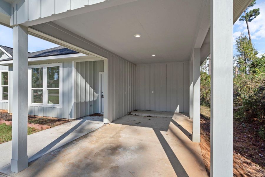 This covered carport area offers convenient, sheltered parking with direct access to the home. The space features clean board-and-batten siding, recessed lighting for nighttime visibility, and plenty of open room for a vehicle or additional storage.