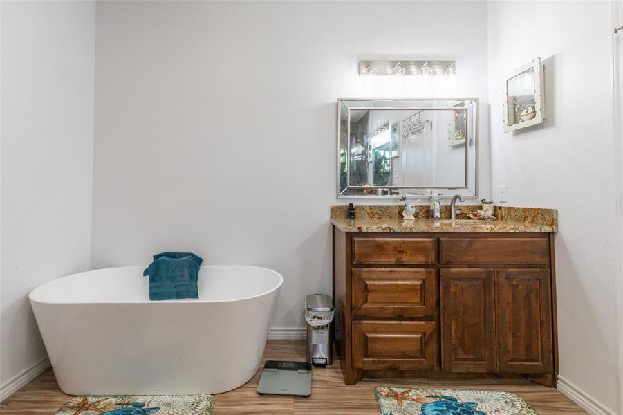 Freestanding soaking tub alongside a wood-finish vanity with a stone countertop, under-mount sink, and a framed wall mirror Freestanding soaking tub alongside a wood-finish vanity with a stone countertop, under-mount sink, and a framed wall mirror