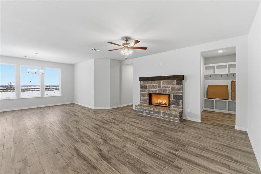 Unfurnished living room featuring wood finish floors, a stone fireplace, ceiling fan, and a chandelier Unfurnished living room featuring wood finish floors, a stone fireplace, ceiling fan, and a chandelier