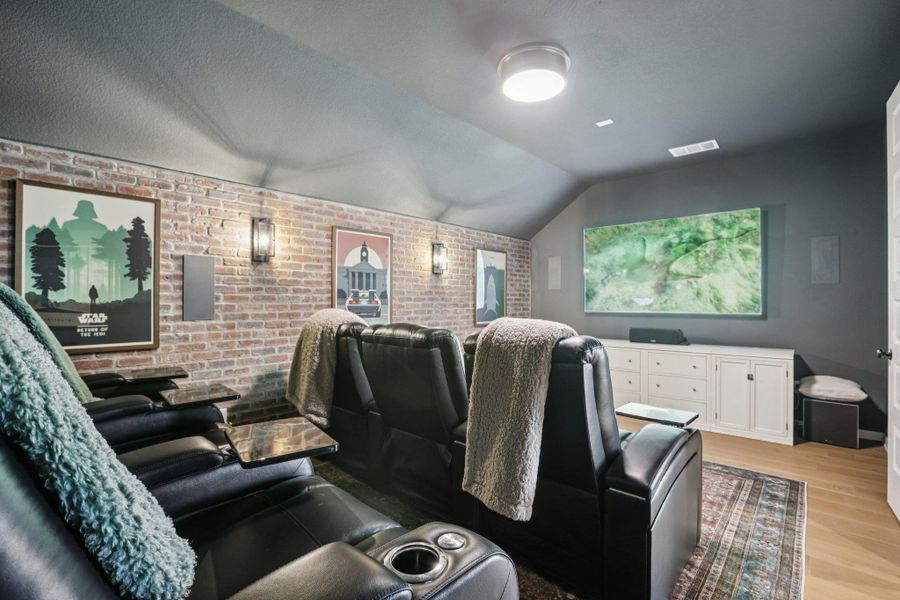 The custom theatre room features an authentic exposed brick wall and comfortable reclined seating for the ultimate cinema experience.
