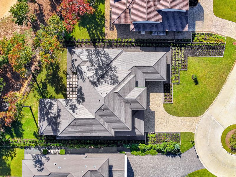 This aerial view shows a modern home with a well-maintained roof and landscaped yard. The property features a spacious driveway, lush greenery, and is located on a quiet cul-de-sac, offering privacy and a suburban feel.