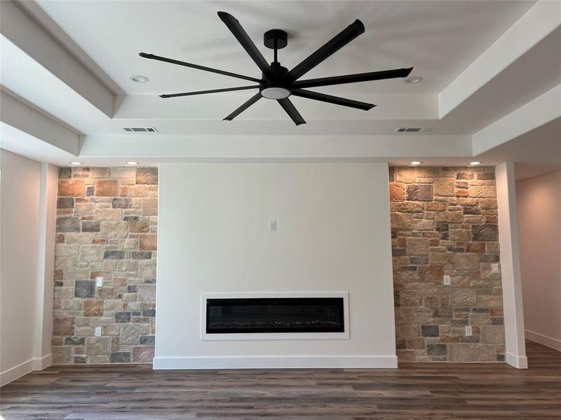 Unfurnished living room with a glass covered fireplace, ceiling fan, a tray ceiling, recessed lighting, and dark wood-type flooring