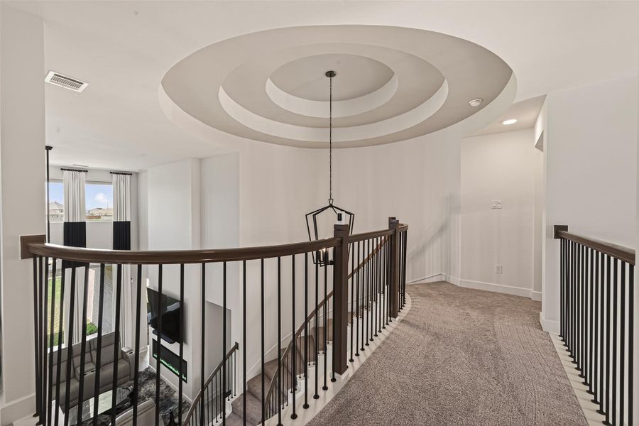 This photo showcases an elegant upstairs landing with a modern circular ceiling design, soft carpeting, and a stylish railing overlooking a bright, open living area below.