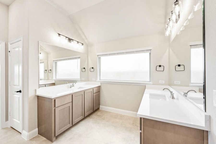 Bathroom with dual vanities, white countertops, tan cabinets, and vaulted ceiling with natural light