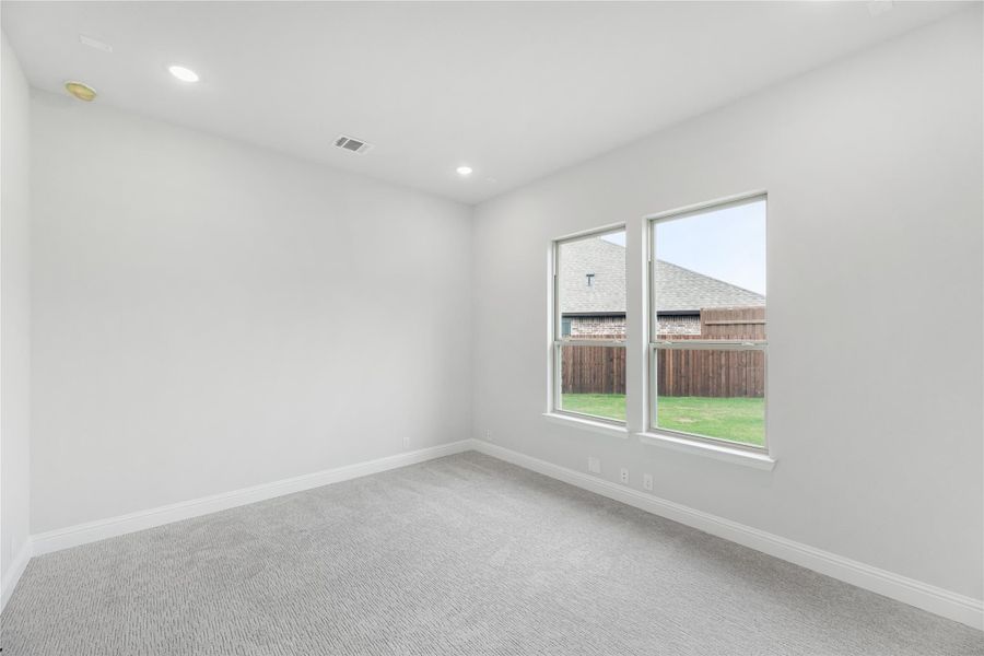 Empty bedroom with gray carpet, white walls, recessed lighting, and two windows overlooking a backyard fence. Empty bedroom with gray carpet, white walls, recessed lighting, and two windows overlooking a backyard fence.