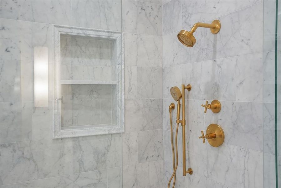 The bathroom features a shower with marble-style tiling, a built-in shower niche, and a modern gold-toned shower system with a handheld showerhead