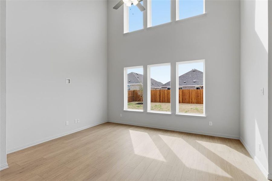 Empty room featuring ceiling fan, light wood finished floors, and a high ceiling