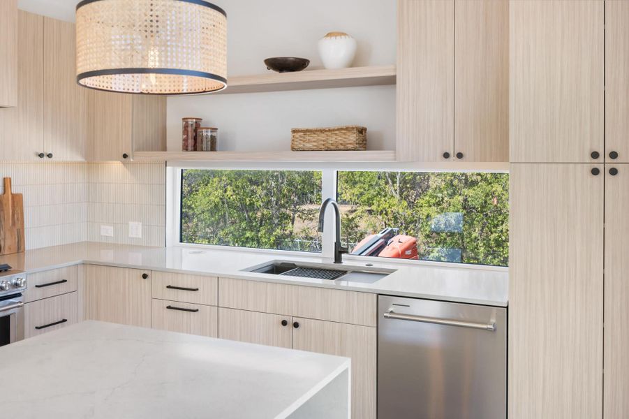 Modern kitchen featuring light wood-finish cabinetry, white countertops, and a full-height window above the sink
