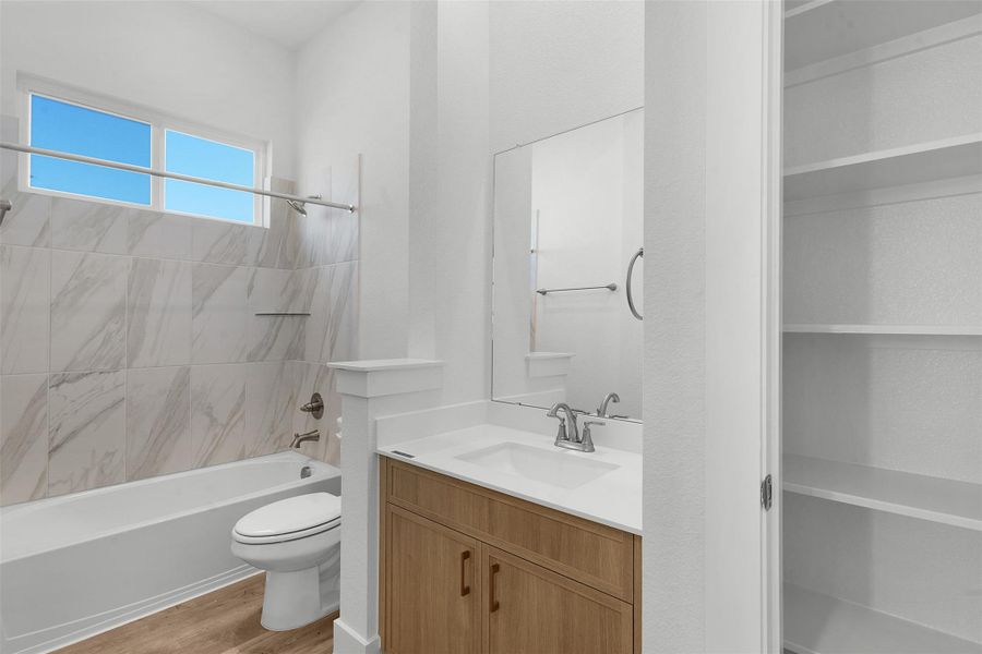 A pristine bathroom featuring sleek wood flooring and a classic tiled shower-tub combination.