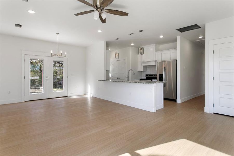 Kitchen featuring light stone countertops, light wood-type flooring, stainless steel appliances, decorative light fixtures, and white cabinetry