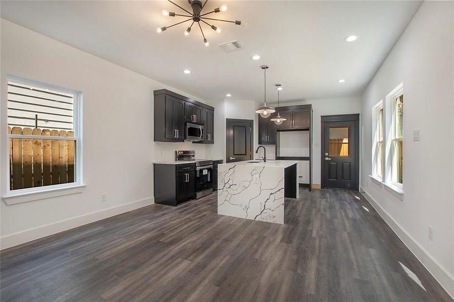 Kitchen with sink, dark hardwood / wood-style flooring, light stone counters, an island with sink, and range with electric cooktop