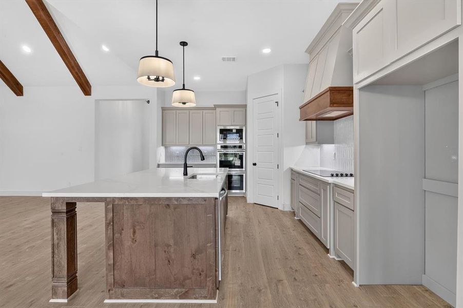 Kitchen featuring a large island with a white countertop and dark wood-finish cabinetry, light grey perimeter cabinetry, and built-in double ovens Kitchen featuring a large island with a white countertop and dark wood-finish cabinetry, light grey perimeter cabinetry, and built-in double ovens