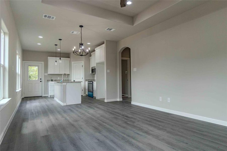 Kitchen featuring a chandelier, white cabinets, hanging light fixtures, hardwood / wood-style floors, and a center island with sink