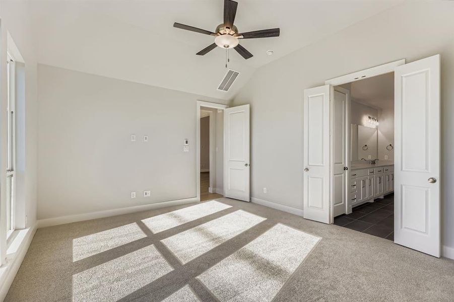 Unfurnished bedroom featuring carpet, vaulted ceiling, ensuite bathroom, and a ceiling fan