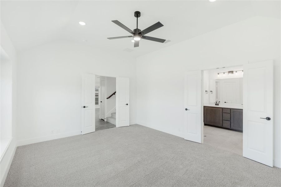 Empty master bedroom with ceiling fan, gray carpet, and open door to ensuite bathroom with dark vanity Empty master bedroom with ceiling fan, gray carpet, and open door to ensuite bathroom with dark vanity