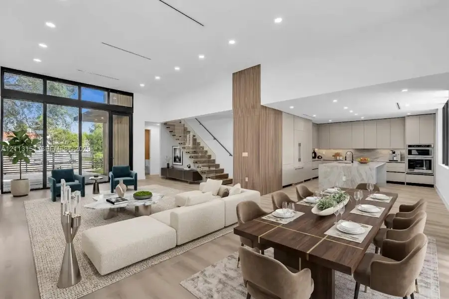 Open-concept interior featuring floor-to-ceiling glass paneling, wood-finish flooring, a kitchen island with natural stone surfacing, integrated cabinetry, and a floating staircase with glass railing Open-concept interior featuring floor-to-ceiling glass paneling, wood-finish flooring, a kitchen island with natural stone surfacing, integrated cabinetry, and a floating staircase with glass railing
