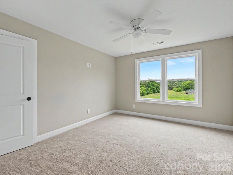 Bright secondary bedroom on upper level features soft carpeting, ceiling fan, and large windows showcasing scenic countryside views.