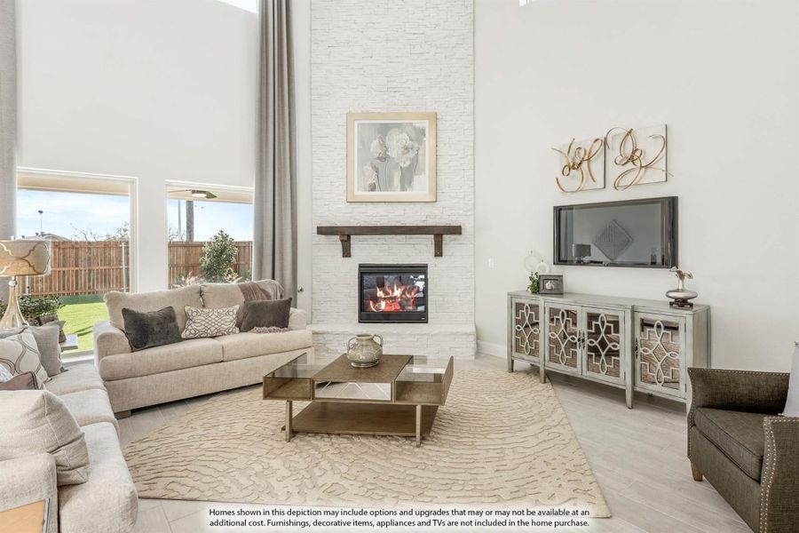 Living room with two-story ceiling, white stone fireplace, neutral sofa, and large windows overlooking backyard