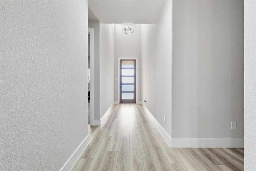 Hall featuring light wood-style floors, a textured wall, and a chandelier