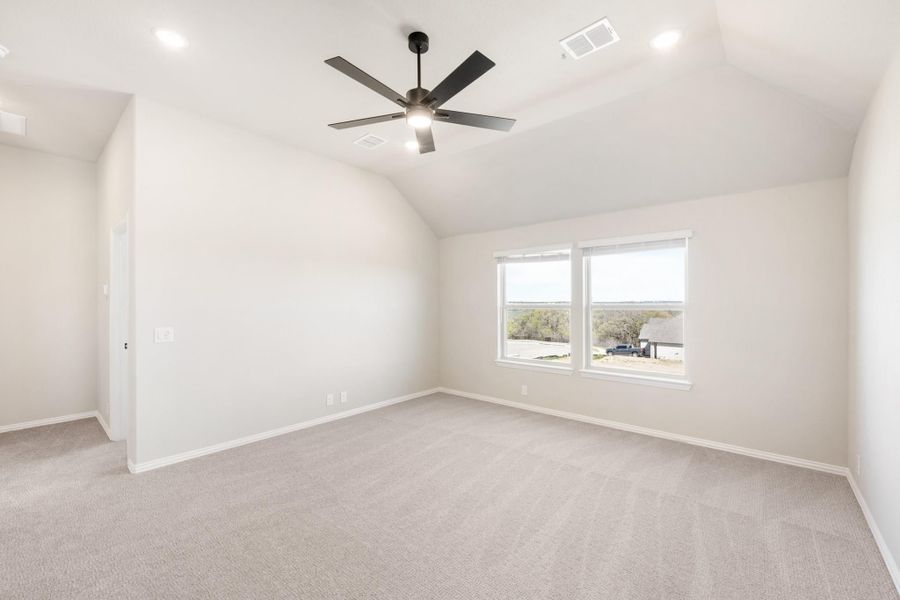 Empty bedroom with vaulted ceiling, ceiling fan, carpet flooring, and double windows