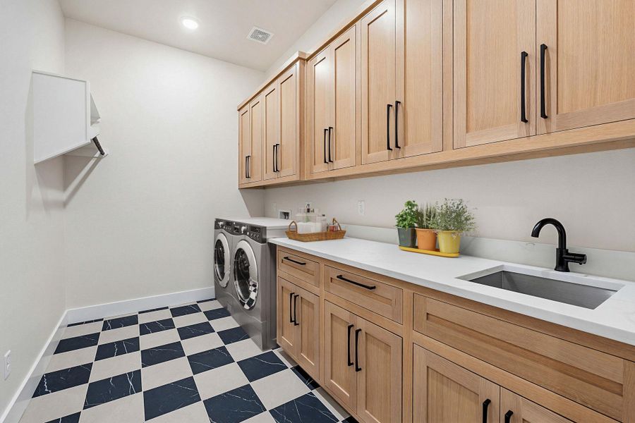 Laundry room featuring light wood cabinetry with black hardware, white countertops, and a black and white tiled floor